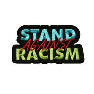 May include: Embroidered patch with the words "STAND AGAINST RACISM" in teal, red, and green. The patch has a black border and is designed to be sewn or ironed onto fabric. The text is in a bold, stylized font.