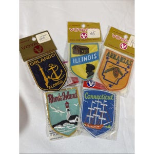 Op de afbeelding: Vijf geborduurde souvenirpatches uit de Voyager World Wide Collectors Series. De patches bevatten ontwerpen voor Orlando Florida, Illinois, Arkansas, Rhode Island en Connecticut, elk verzegeld in een individuele doorzichtige verpakking.