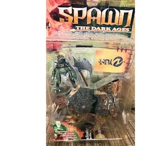 May include: Spawn The Dark Ages action figure set in original packaging. Includes a green creature figure, a brown beast with armour, a grey battle axe, and a banner. The packaging features the text Spawn The Dark Ages and Gigantus can sit on saddle tuskadon has bendy tail.