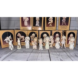 May include: A collection of ten small porcelain figurines, each accompanied by its original tan cardboard box. The figurines depict various children and animals in muted tones, including a unicorn, a rocking horse, and several figures in winter clothing.