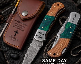 May include: A brown leather sheath with a metal snap, engraved with a cross and the text Godparents are a blessing, thank you for being mine, Joshua 10.12.2025. Two folding knives with wood and green resin handles and Damascus steel blades.