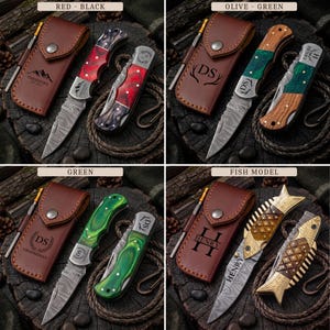 May include: Four sets of folding pocket knives with Damascus steel blades and matching leather sheaths. Each set features personalized engravings on the blade and sheath, including names and initials. The handles vary in color and shape, including red, green, and fish-shaped designs, displayed on a dark wood surface.