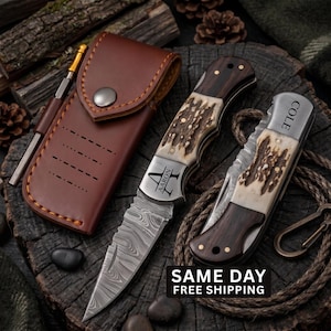 May include: Two folding knives with Damascus steel blades and handles featuring dark wood and textured antler inlays. One knife is open, engraved with the name AARON, and the other is closed, engraved with COLE. Includes a brown leather sheath.