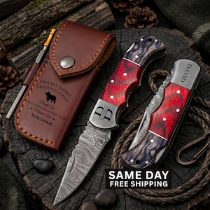 May include: Two folding pocket knives with red and black marbled handles and Damascus steel blades, one featuring the name David and the other the initials DD, alongside a brown leather sheath engraved with text including Kevin Livestock.