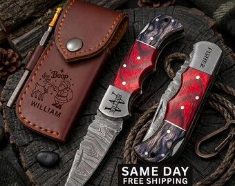 May include: Two folding pocket knives with red and black marbled handles and Damascus steel blades, one engraved with WILLIAM, alongside a brown leather sheath featuring a Santa Claus graphic and the text Boop WILLIAM.