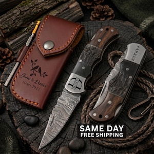 May include: Two folding knives with Damascus steel blades and dark wood handles, one featuring the name Parker and the other the name Dustin. A brown leather sheath is engraved with the text Jane & Dustin 10.09.2021 and a bird design.