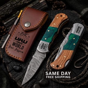 May include: A brown leather sheath with a metal snap and the text Best Dad in the World Love, Jessica, a folding knife with a Damascus steel blade, wood and green resin handle, and a second folded knife engraved with My First Hero David Johnson.