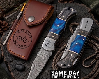 May include: Two folding pocket knives with Damascus steel blades and blue and black wood handles, one engraved with the name Connor and the other with Sean, alongside a brown leather sheath embossed with a bicycle and the text RIDE BIKES BE HAPPY.
