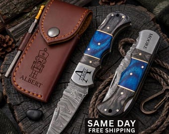 May include: A brown leather sheath with a nutcracker graphic and the name ALBERT, a folding knife with a Damascus steel blade and blue and black wood handle engraved with ALBERT, and a second folding knife with a blue and black handle engraved MOORE.