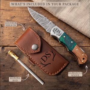 May include: A Damascus steel folding knife with a green and wood handle, a brown leather sheath, and a metal honing rod. The knife blade and sheath are engraved with the letters DS and antler icons. Text reads: WHAT'S INCLUDED IN YOUR PACKAGE.