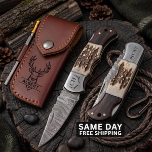 May include: Two folding knives with Damascus steel blades and antler and wood handles, one open and one closed. The closed knife is engraved with the name JACOB. The open knife features the initials CH. A brown leather sheath displays a deer head and the name ALBERT.