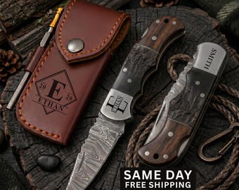 May include: Two folding pocket knives with Damascus steel blades and wood handles, one open and one closed, alongside a brown leather sheath. The sheath features a diamond logo with the letter E, the name ETHAN, and the year 2026. One knife is engraved with ETHAN, the other with SMITH.