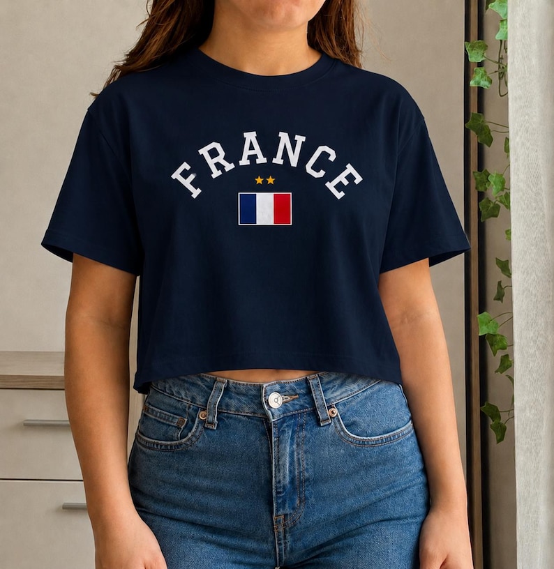 May include: Navy blue crop top with the word "FRANCE" in white arched lettering. Below the word is a small French flag and two gold stars. The shirt is paired with blue jeans.
