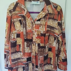 May include: A long-sleeve button-down shirt featuring a geometric abstract pattern in shades of burnt orange, dark brown, tan, and white. The shirt has a pointed collar and a label at the neckline that reads Berkshire. The front includes five buttons.