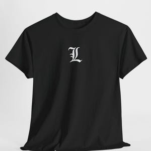 May include: Black t-shirt featuring a white, ornate letter "L" on the front. The short-sleeved top has a crew neck and is made from a soft fabric. The letter is centrally placed on the chest.