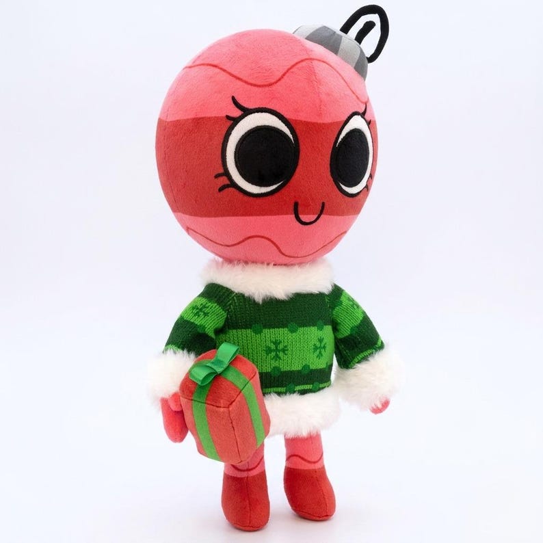 K&ouml;nnte beinhalten: Ein Pl&uuml;sch-Weihnachtsschmuck-Charakter mit einem l&auml;chelnden Gesicht, der einen gr&uuml;nen Pullover mit wei&szlig;em Besatz tr&auml;gt und eine rote Geschenkbox h&auml;lt. Der Schmuck ist rosa und rot mit schwarzen Augen und einem grauen Oberteil.
