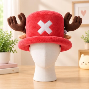 May include: A bright red plush hat featuring a large white X symbol on the front and two brown, soft-textured reindeer antlers extending from the sides. The hat has a wide, rounded brim and a cylindrical crown, crafted from a soft, fuzzy material.