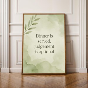 May include: A framed wall art print featuring a pale green watercolor background with a leafy branch illustration in the top left corner and the text Dinner is served, judgement is optional printed in dark gray in the center.