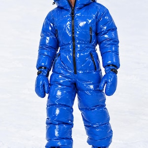 Può includere: Una tuta da neve isolante intera, lucida e di colore blu brillante, dotata di collo alto, cappuccio con fodera interna rossa, chiusura frontale con zip, oltre a muffole e stivali blu abbinati. Il capo presenta una struttura trapuntata.