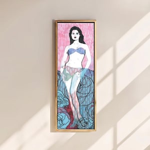 Puede incluir: Una pieza de arte mural rectangular vertical enmarcada que presenta una ilustración estilizada de una persona con cabello oscuro que viste un top de bikini azul y una parte inferior estampada. El fondo consta de líneas verticales rosas y grandes formas florales azules.