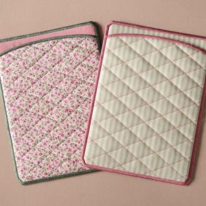 May include: Two rectangular quilted fabric sleeves. The left sleeve features a pink floral pattern with a green border. The right sleeve features a light green and white vertical stripe pattern with a pink border. Both have diamond stitching.
