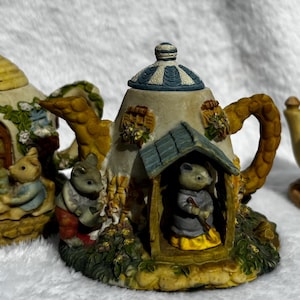 Può includere: Tre statuette decorative in ceramica a forma di teiera con personaggi di topi antropomorfi. Ogni pezzo presenta dettagli complessi tra cui porte, finestre, piante rampicanti e piccoli topi impegnati in varie attività.
