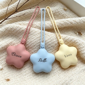 May include: Three star-shaped silicone pacifier clips in dusty rose, light blue, and pale yellow. Each clip features a long, flexible loop with a small star detail at the base and is personalized with the names Elowen, Belle, and Liora in black.