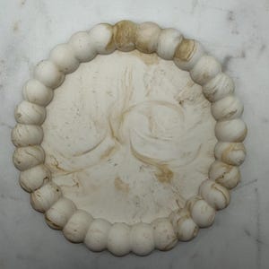 Puede incluir: Una bandeja circular con un centro plano y liso que presenta un patrón jaspeado en blanco y bronceado. El borde exterior está definido por un reborde elevado y continuo compuesto por esferas redondeadas con el mismo acabado jaspeado.