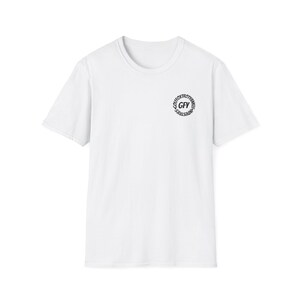 以下が含まれることがあります： 白いクルーネックTシャツ。左胸に小さな円形のグラフィックがあります。グラフィックは、中央に「GFY」の文字、周りに「GOLFTROXTROTYANKEE INDUSTRIES」の文字が配置されています。