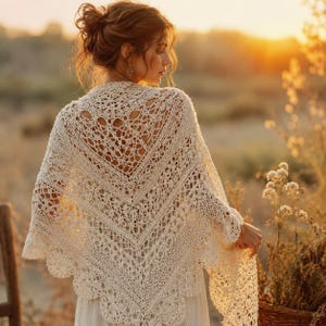 Peut inclure: Un châle triangulaire de couleur crème présentant un motif complexe en crochet ajouré avec un bord festonné. Le vêtement est drapé sur les épaules, mettant en valeur un design en dentelle détaillé avec des motifs géométriques et floraux.