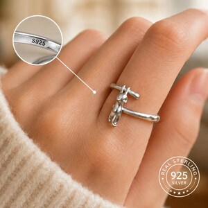 May include: A sterling silver ring featuring a cat design. The ring is stamped with "S925" and "REAL STERLING 925 SILVER". The cat is depicted in a stylized form, with a simple, elegant design. The ring is worn on a finger.