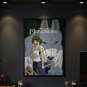 May include: A framed poster featuring the title Princess Mononoke in white text. The artwork displays a character with short green hair, a white top, and a dark skirt, holding a knife. Behind the character is a large white wolf with dark eyes.
