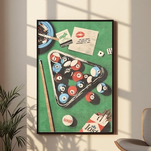 May include: A framed poster featuring a green pool table surface with a triangular rack of billiard balls spelling out "lost in america". The scene includes a pool cue, a pack of cigarettes, a matchbook, a lipstick kiss, and dice.