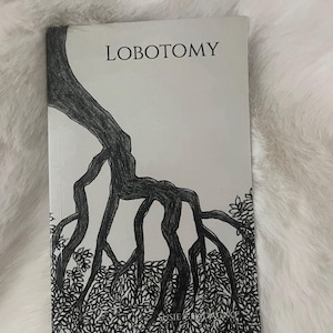 Op de afbeelding: Een boek getiteld "LOBOTOMY" met een zwart-wit illustratie van boomwortels en bladeren. De cover bevat een gedetailleerde tekening van het wortelstelsel van een boom dat zich over de cover uitstrekt, met de titel bovenaan.