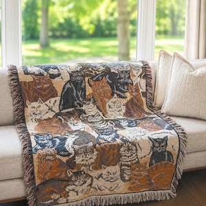 May include: A woven throw blanket featuring a repeating pattern of various cat breeds in shades of brown, black, white, and tan. The rectangular textile has a decorative fringed edge along the sides and bottom, showcasing a detailed feline motif.