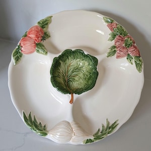 Peut inclure: Un plat de service divisé en céramique de couleur crème avec trois sections. Le centre est orné d'une feuille de chou verte en relief. Le bord est décoré de détails sculptés et peints à la main, incluant des radis roses, des feuilles vertes et des bulbes d'ail blancs.