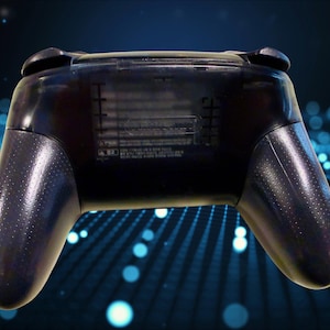 K&ouml;nnte beinhalten: Ein durchscheinend schwarzer kabelloser Videospiel-Controller von der R&uuml;ckseite gesehen. Das Ger&auml;t verf&uuml;gt &uuml;ber einen strukturierten Griff an beiden Seiten und ein zentrales Batteriefach mit schwach gepr&auml;gtem Text und sichtbaren Kennzeichnungen.