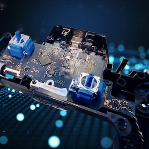 K&ouml;nnte beinhalten: Eine freiliegende interne Leiterplatte eines Videospiel-Controllers mit zwei blauen analogen Stick-Modulen, verschiedenen Mikrochips und integrierten elektronischen Komponenten, die auf einer dunkelgr&uuml;nen Platine in einem schwarzen Kunststoffgeh&auml;use montiert sind.