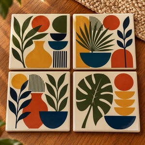 May include: A set of four square ceramic coasters featuring graphic illustrations of potted plants, vases, and geometric shapes in a palette of orange, yellow, dark green, and navy blue on an off-white background.