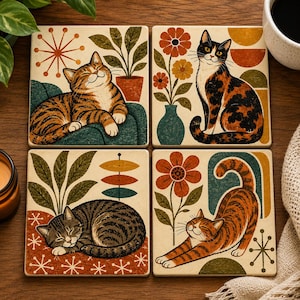 May include: A set of four square coasters featuring illustrations of cats in various poses. The designs include a tabby cat on a sofa, a calico cat near a flower vase, a sleeping tabby cat, and a stretching orange tabby cat with floral and geometric motifs.