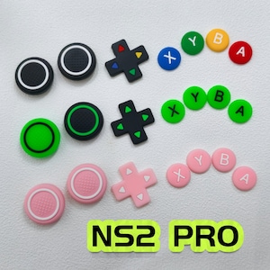 May include: A set of replacement controller parts for NS2 PRO including three D-pads, six analogue stick covers, and twelve action buttons labelled X, Y, B, and A. The components come in black, green, and pink colour sets with varied accent colours.