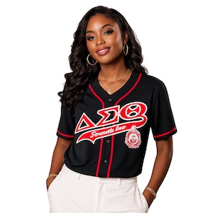 May include: A black short-sleeved baseball jersey featuring red trim along the V-neck and sleeves. The front displays the Greek letters Delta Sigma Theta in white with red outlines, the text Sororite Inc, and a circular red and white emblem on the chest.