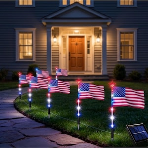 May include: A series of solar-powered garden stakes featuring miniature American flags. Each stake has a red, white, and blue light-up pole topped with a red star. The flags are illuminated and arranged along a stone walkway in a grassy yard.