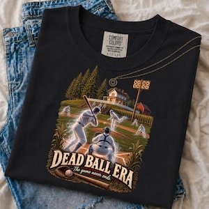 May include: A black t-shirt featuring a graphic of baseball players in a field with a house in the background. The text reads "DEAD BALL ERA" and "The game never ends." A baseball glove and ball are at the bottom. The shirt has a Comfort Colors label.