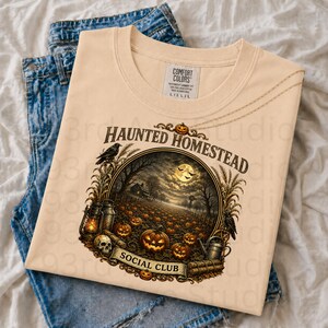 May include: A beige t-shirt featuring a circular graphic with the text "HAUNTED HOMESTEAD SOCIAL CLUB". The illustration depicts a pumpkin patch at night under a full moon, with a skull, a lantern, a watering can, and crows in the frame.