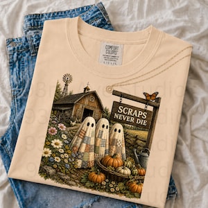 May include: A light beige t-shirt featuring a graphic of three ghosts covered in colorful patchwork quilts standing in a field with a barn, a wooden sign that reads SCRAPS NEVER DIE, a butterfly, pumpkins, and a watering can in the foreground.