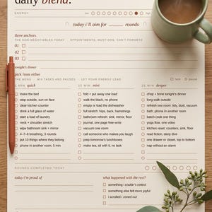 Könnte beinhalten: Ein beigefarbener Tagesplaner mit dem Text "daily blend" und Kontrollkästchen für Aufgaben. Eine Tasse Kaffee und ein Stift befinden sich auf der rechten Seite. Der Planer enthält Abschnitte für Energielevel und absolvierte Runden.