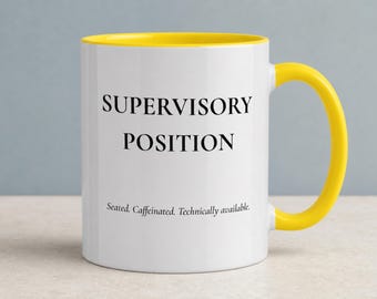 May include: A white ceramic mug with a bright yellow interior and handle. The front features the black text SUPERVISORY POSITION in a bold serif font, followed by the smaller text Seated. Caffeinated. Technically available. in a standard font.
