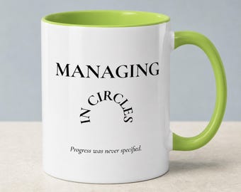May include: A white ceramic mug with a lime green interior and handle. The front features black text that reads "MANAGING" at the top, "IN CIRCLES" in a curved arc in the middle, and "Progress was never specified." at the bottom.