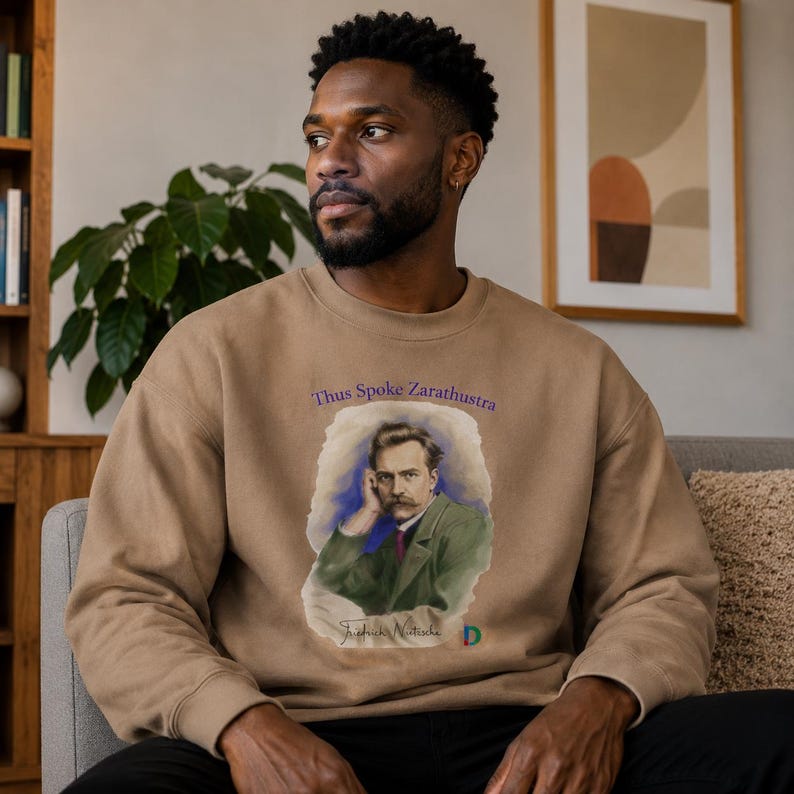 Peut inclure: Un sweat-shirt &agrave; col rond beige avec une impression graphique de Friedrich Nietzsche portant une veste verte. Le texte "Thus Spoke Zarathustra" est imprim&eacute; en violet au-dessus du portrait, avec le nom "Friedrich Nietzsche" &eacute;crit en cursif.